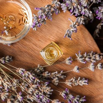 Glassware with essential oil and lavender on wooden board